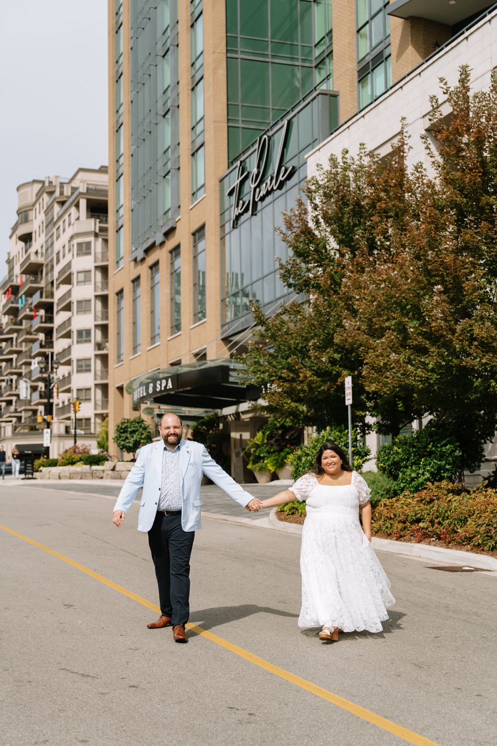 Angela and Michael walking hand in hand down a city street lined with trees