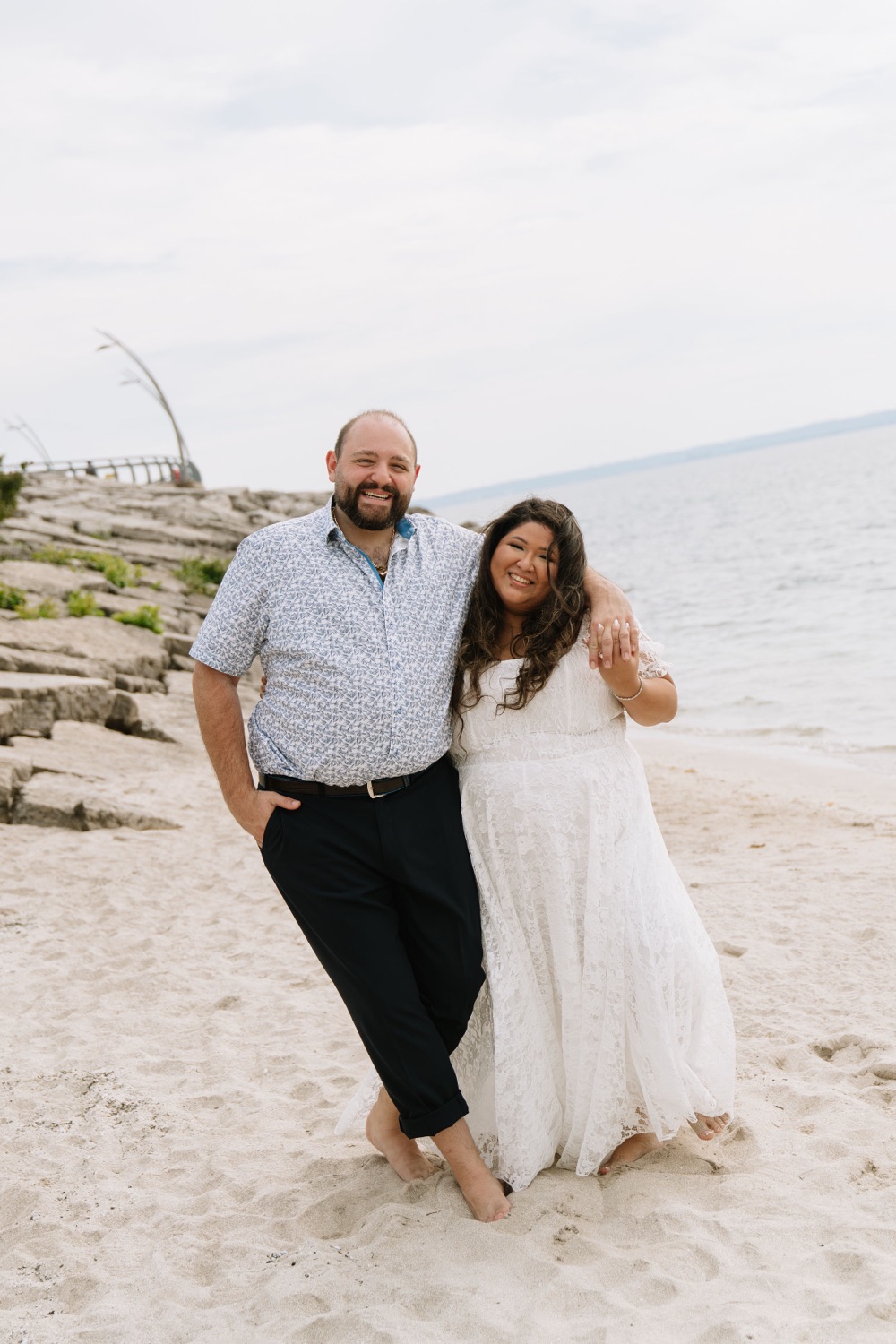 Angela and Michael smiling together on a sandy beach by the lake