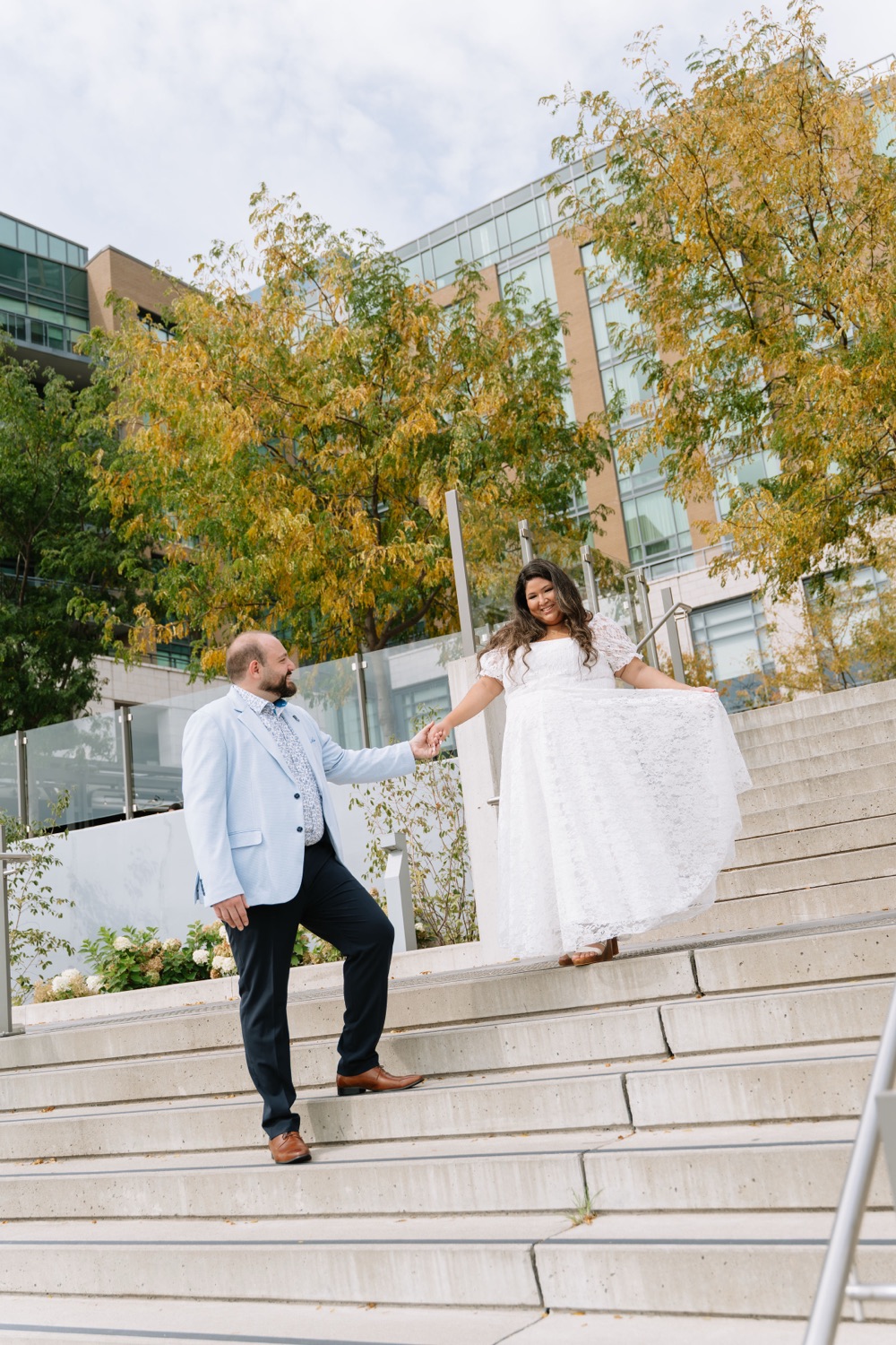 Michael leading Angela by the hand down a flight of city stairs among autumn trees
